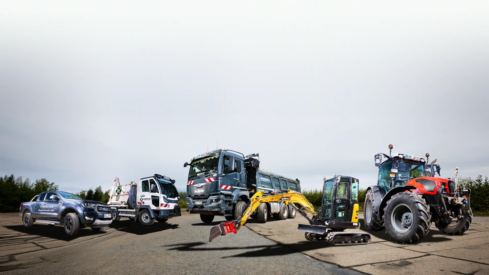 Der Fuhrpark der Findeklee Gruppe auf dem Betriebshof: Pickup, Absetzkipper, MAN-Kipper, Minibagger und Traktor